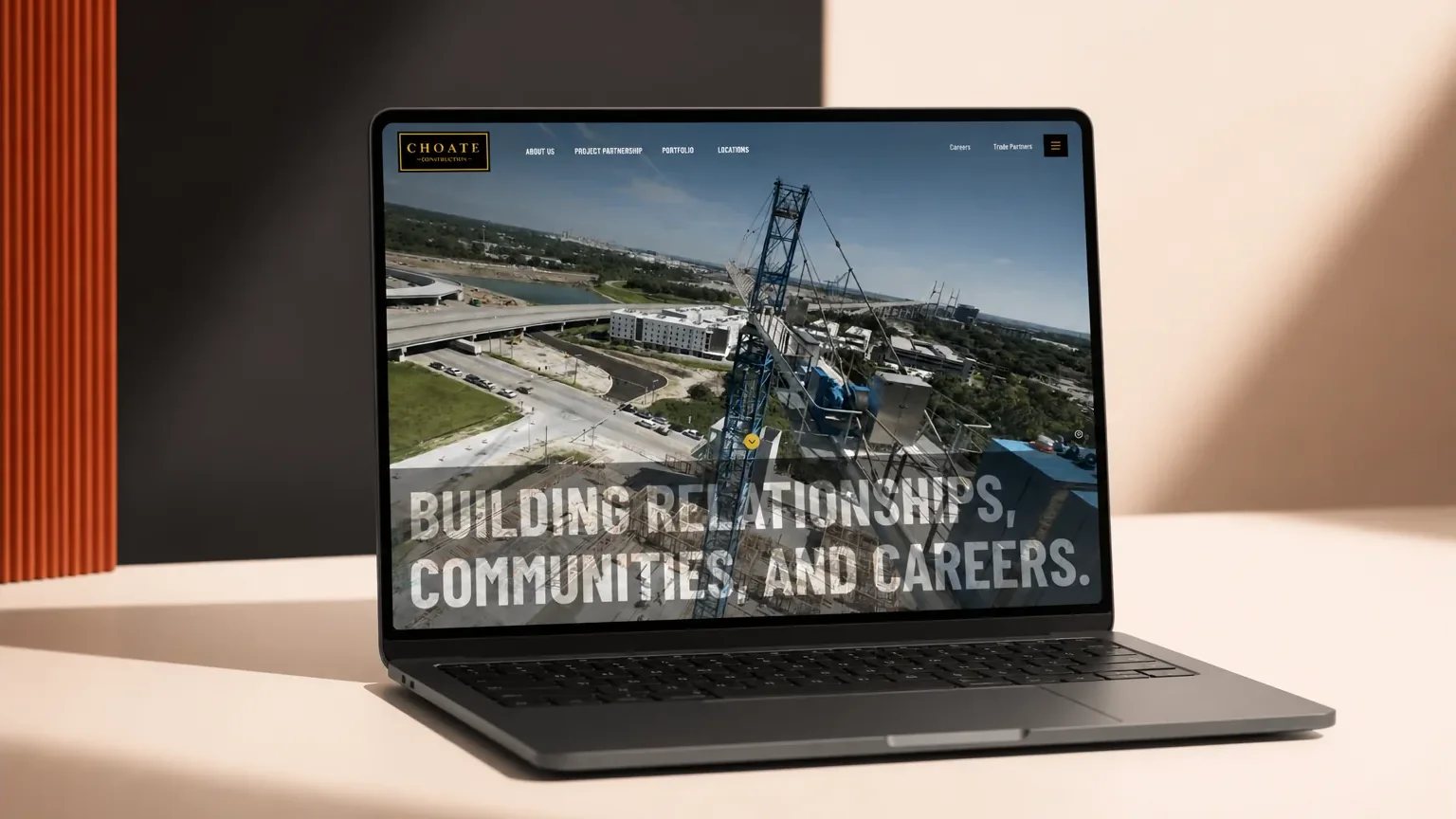Choate Construction homepage displayed on a laptop against a peach, charcoal, and orange studio backdrop.