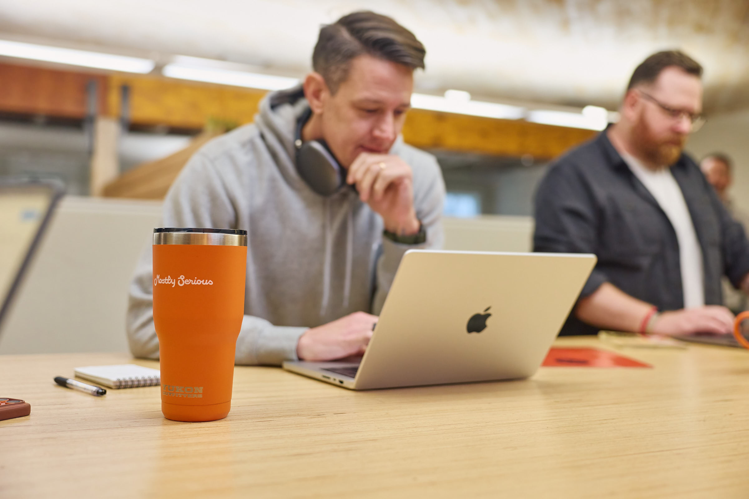 Two Mostly Serious team members working together on laptops at a standing table.